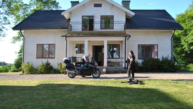 2 people standing outside Berglunda hostel with a motorcycle.