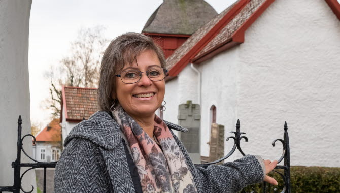 Kvinna som står vid grinden in till en vit liten kyrka med rött tak.