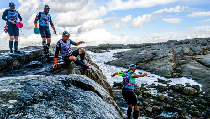 Fyra personer i våtdräkt springer över berget, de deltar i Swimrun på Öckerö