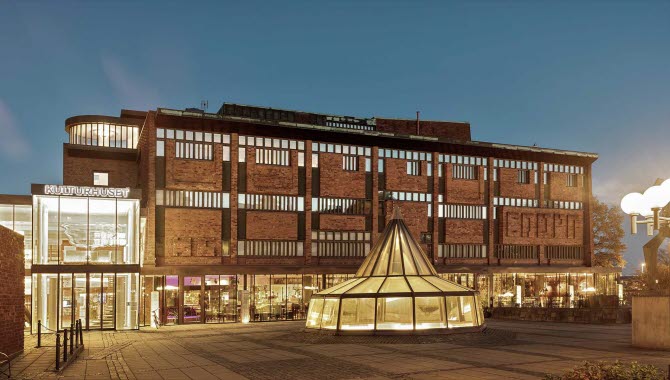 Skövde Kulturhus i kvällsskrud. Från alla fönster i tegelhuset lyser ett varmt gult ljus.