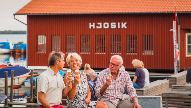 Tre människor äter glass i Hjo hamn, med fiskaffären Hjo Sik i bakgrunden.