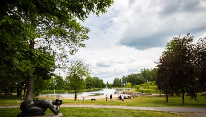 Grönska och staty i en park. I bakgrunden ligger badsjön Boulognersjön