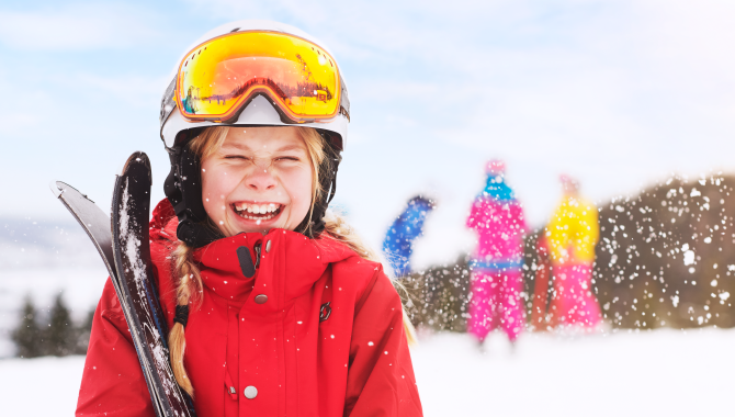 Ett barn i färgglada kläder med skidor i famnen på toppen av Ulricehamn Ski Center.