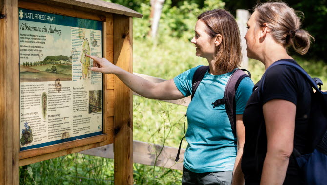 Två kvinnor står och läser på en skylt om naturreservatet.