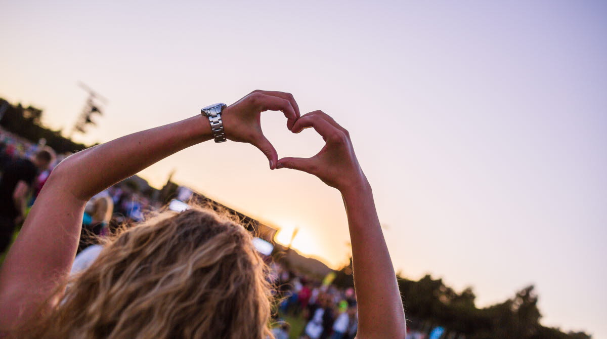 En kvinnlig åskådare på en konsert sträcker upp sina armar i luften och bildar ett hjärta med sina händer.