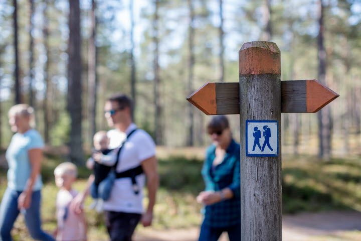 En familj vandrar på Hökensås naturområde.En vägvisare visar vägen.