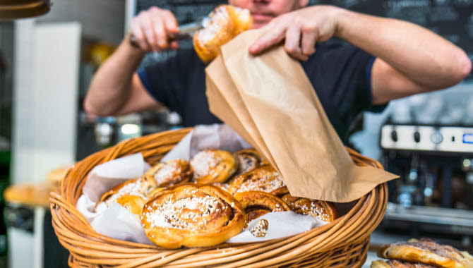 Caféägare lägger i nybakta bullar i en påse.