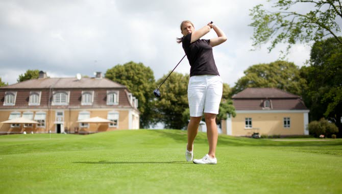 En kvinna står och har precis slagit iväg sin golfboll på golfbanan vid Bjertorp i Vara.