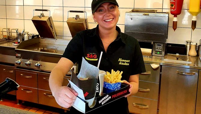Hammarkioskens personal håller upp en bricka med pommes, dricka och hamburgare.