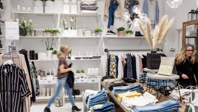 En ljus och fräsch butik med jeans uppradade på ett bord. I butiken finns hyllor med vita inredningsdetaljer. Två kvinnor kikar runt i butiken.