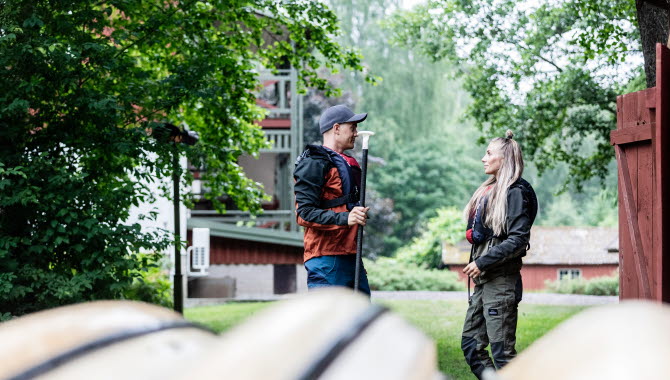 En kvinna och en man står i med var sin paddel i förgrunden syns några kanoter.