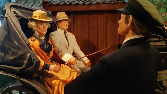 Ett par sitter i en vagn, en man står framför i uniform.