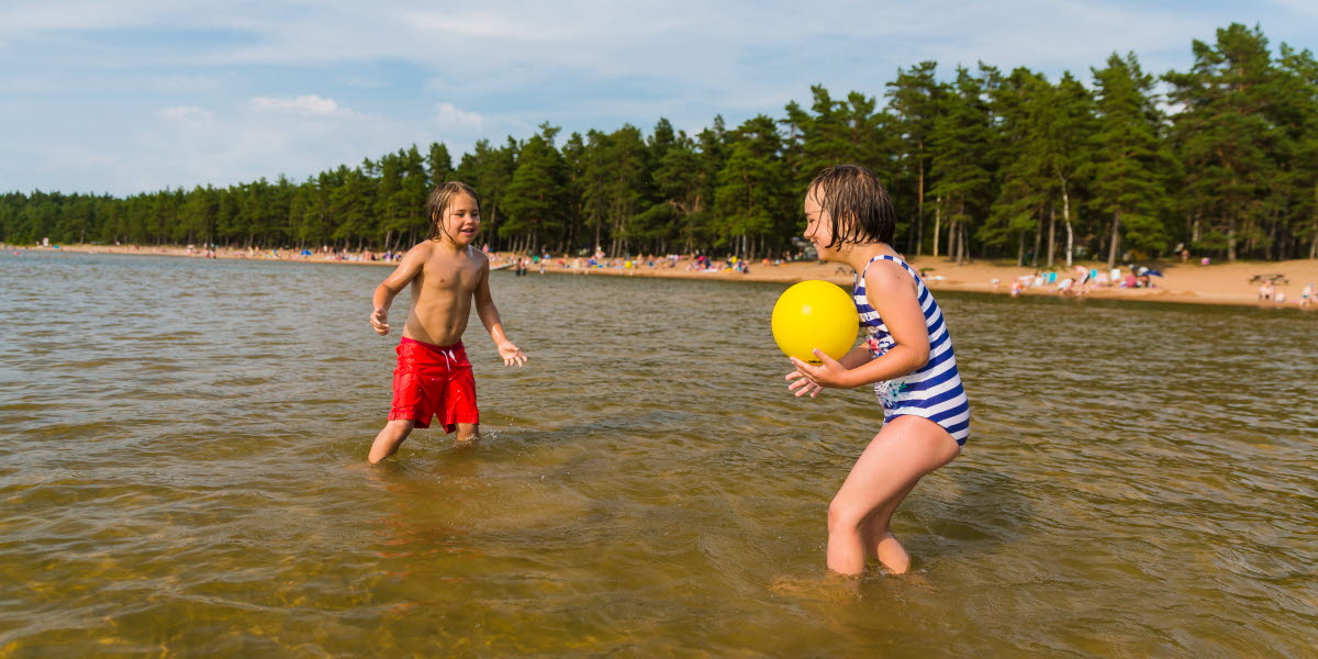 En pojke och en flicka kastar boll till varandra i vattnet.