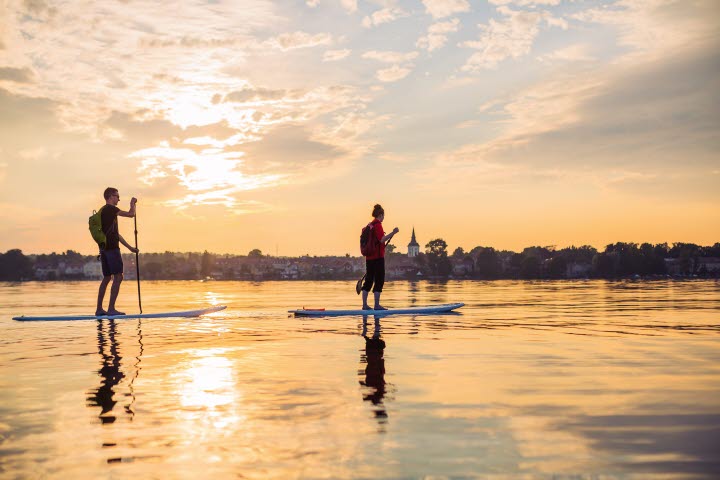Two people are slowly paddling on a Stand up paddleboard on lake Vättern. 