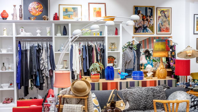Butiksbild tagen i en second hand-butik. På bilden finns äldre möbler, en designlampa och vintagekläder.