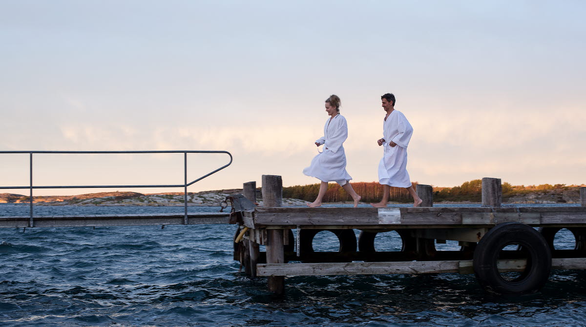 Två personer i badrock på en brygga vid havet.